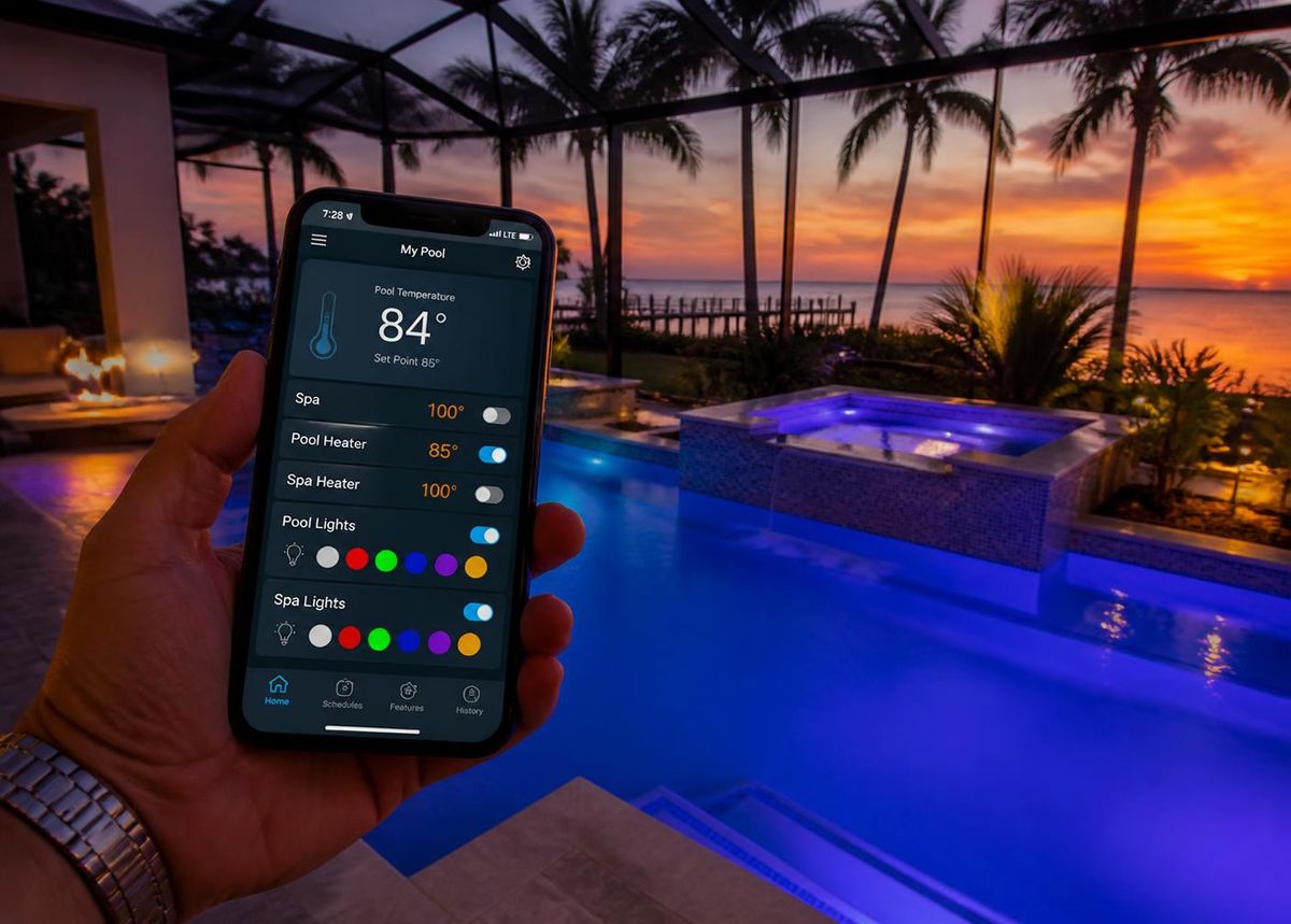 Phone running a pool automation app beside a lit pool at Florida sunset